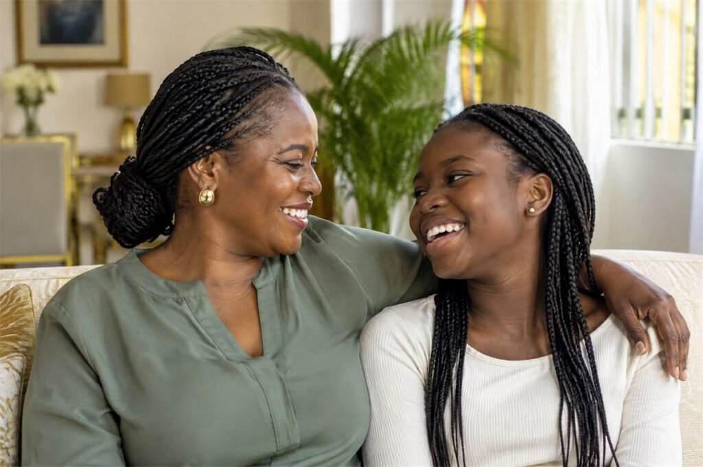 A mother and her teenage daughter laughing together on a sofa at home